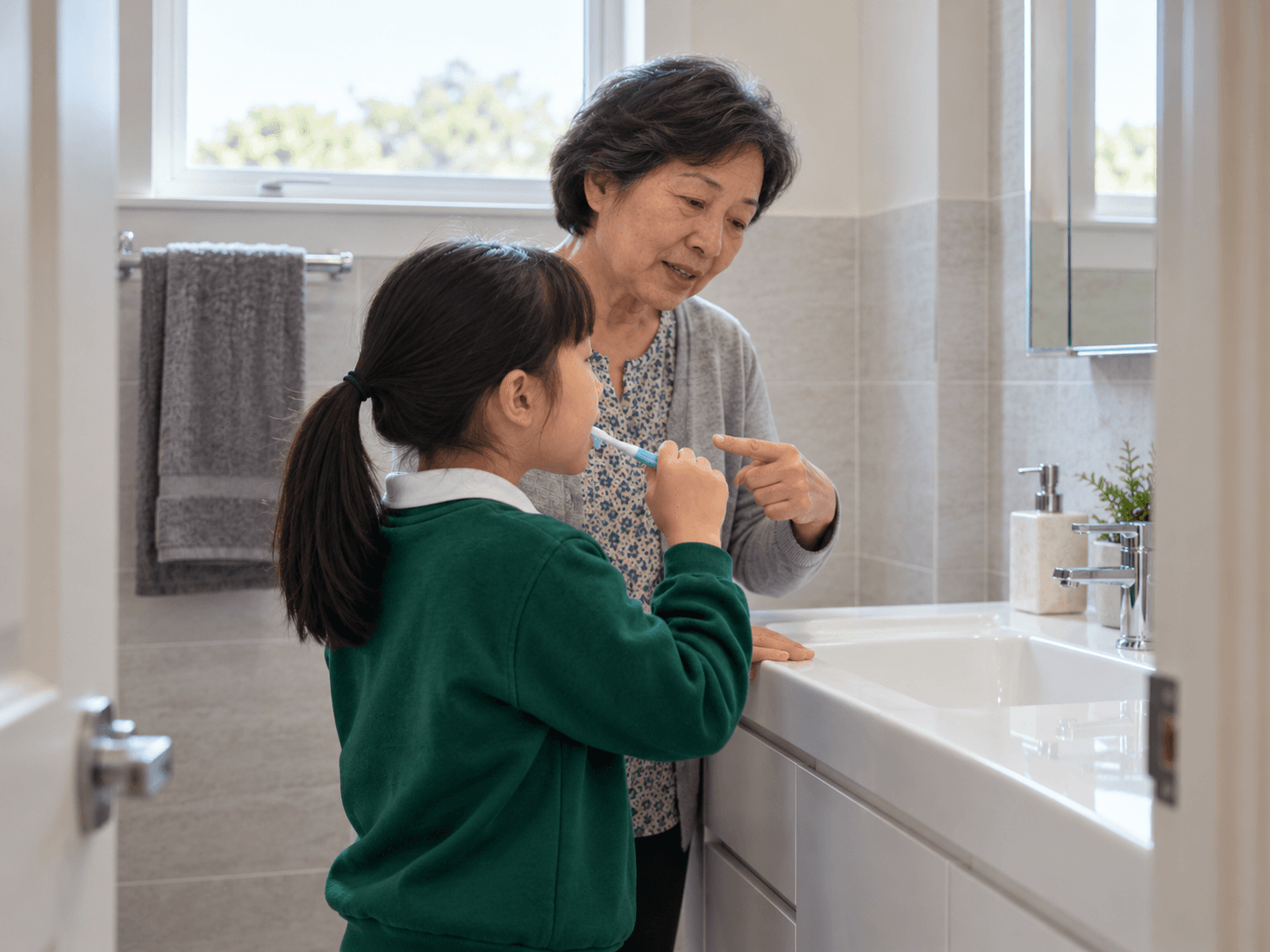 A grandmother watches a child brush while they discuss reaching the changing front teeth.