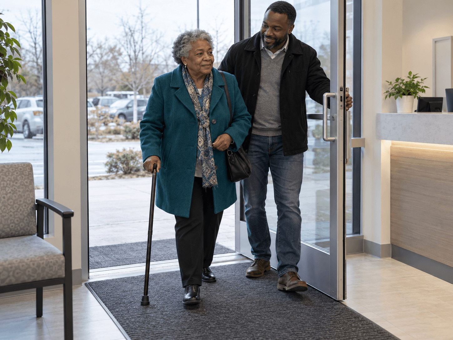 A woman using a walking cane enters a dental clinic while a companion holds the door.
