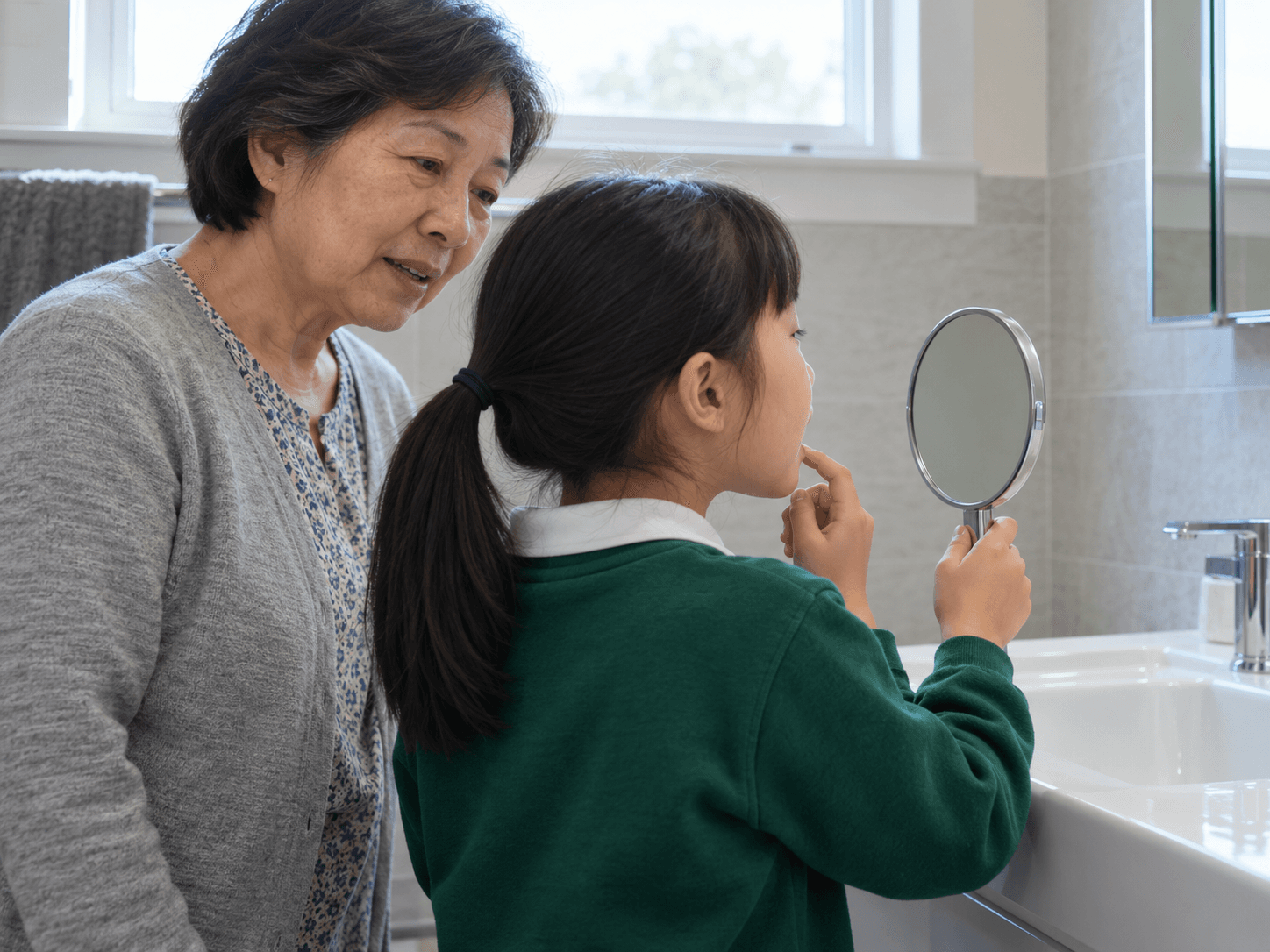 A child looks in a hand mirror while talking with her grandmother about a new tooth.