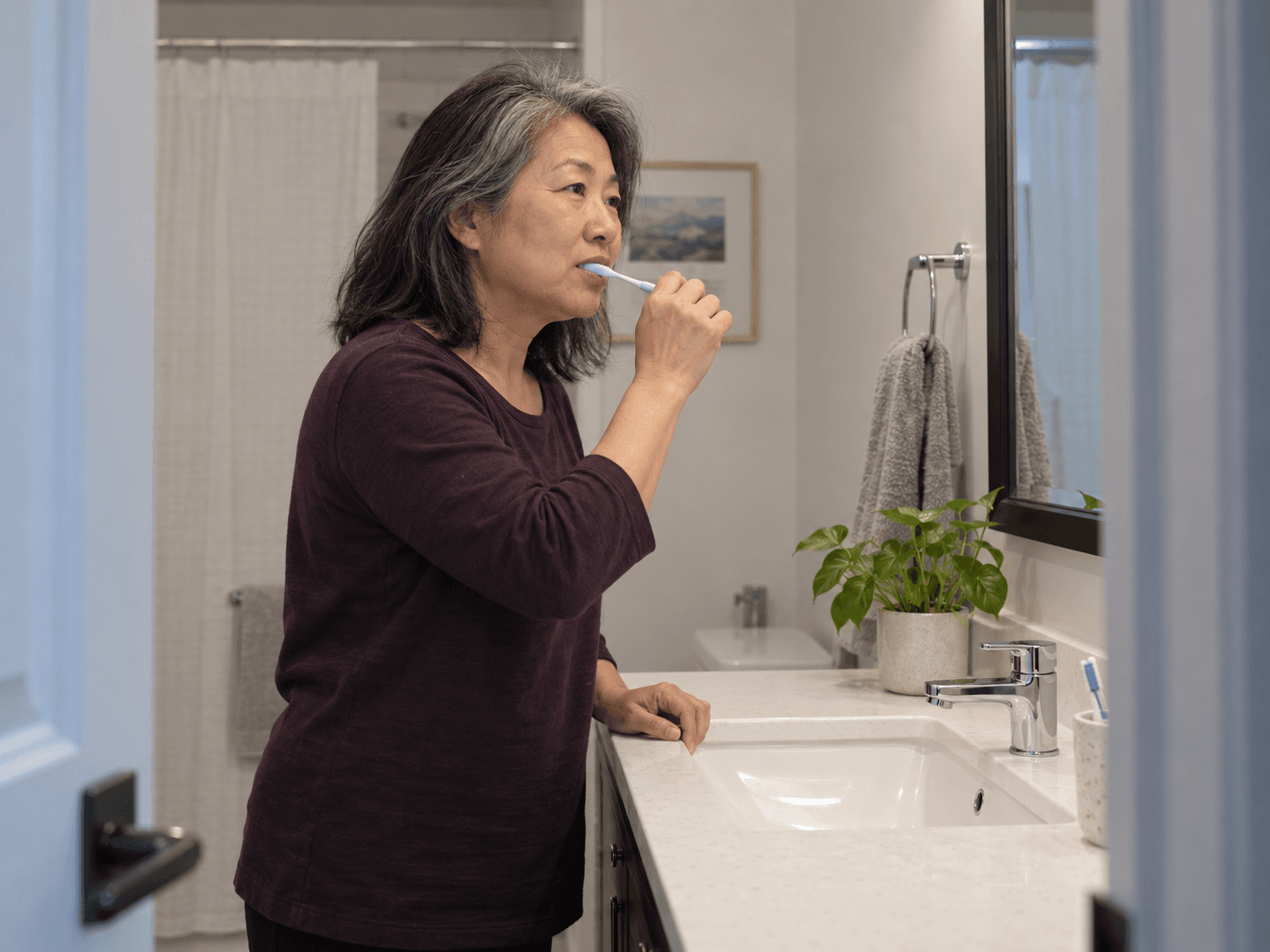 A woman gently brushes at her bathroom sink as part of her daily mouth-care routine.