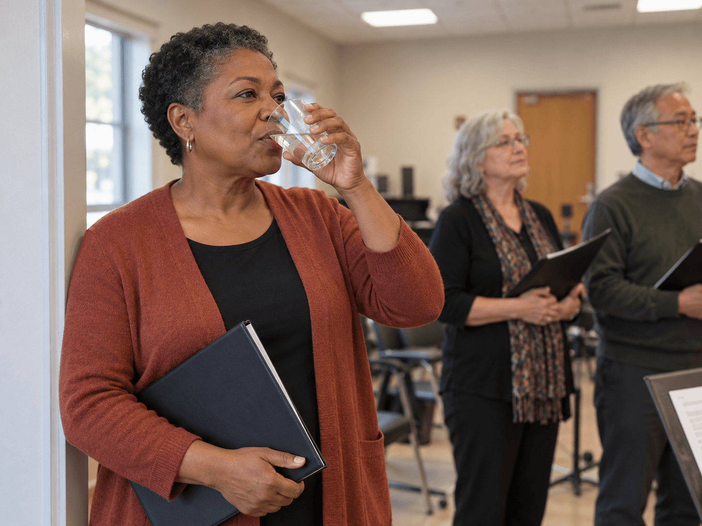 A woman pauses for a sip of water during a community choir rehearsal.