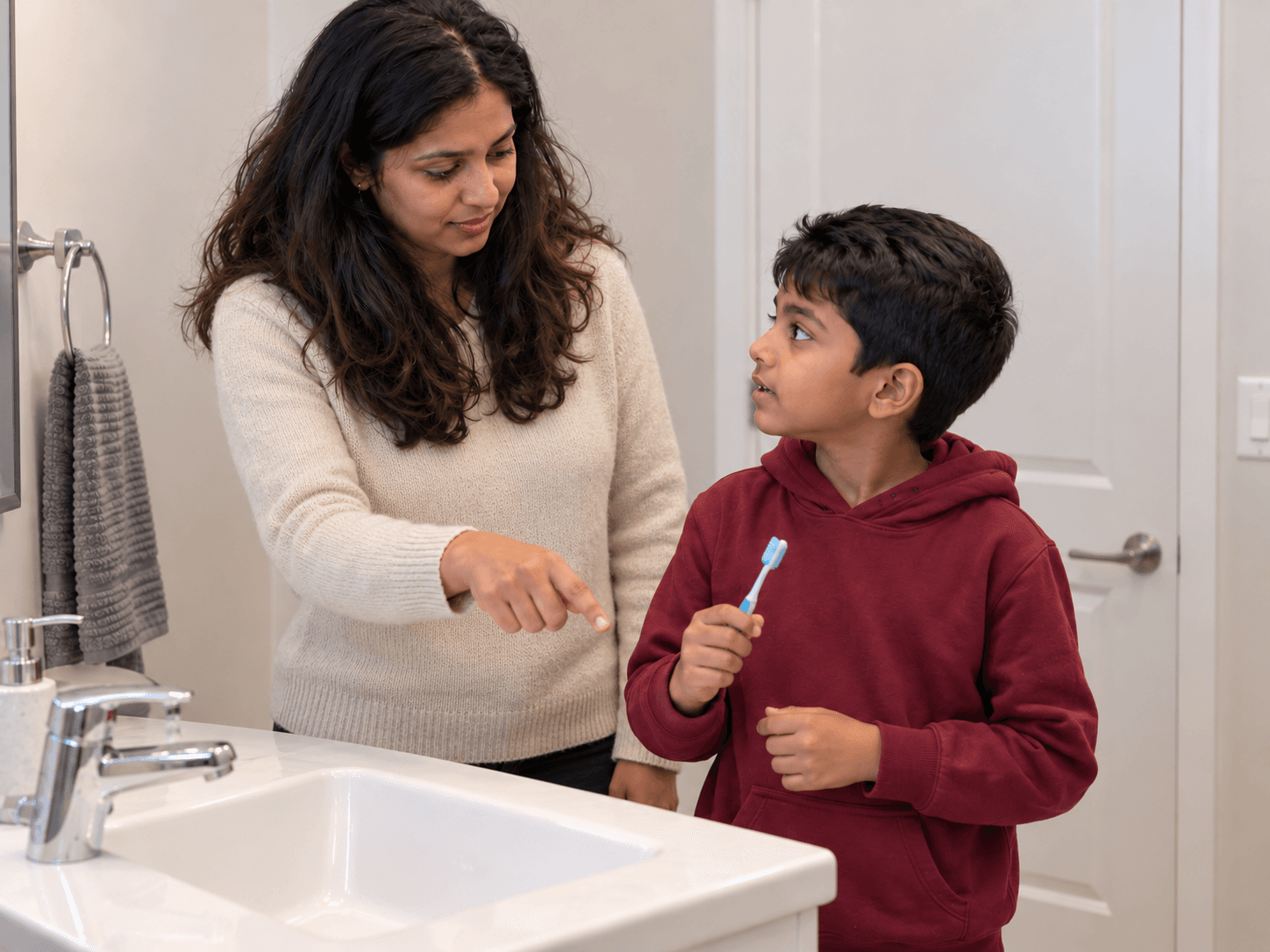 A mother and son discuss their cleaning routine beside the bathroom sink.