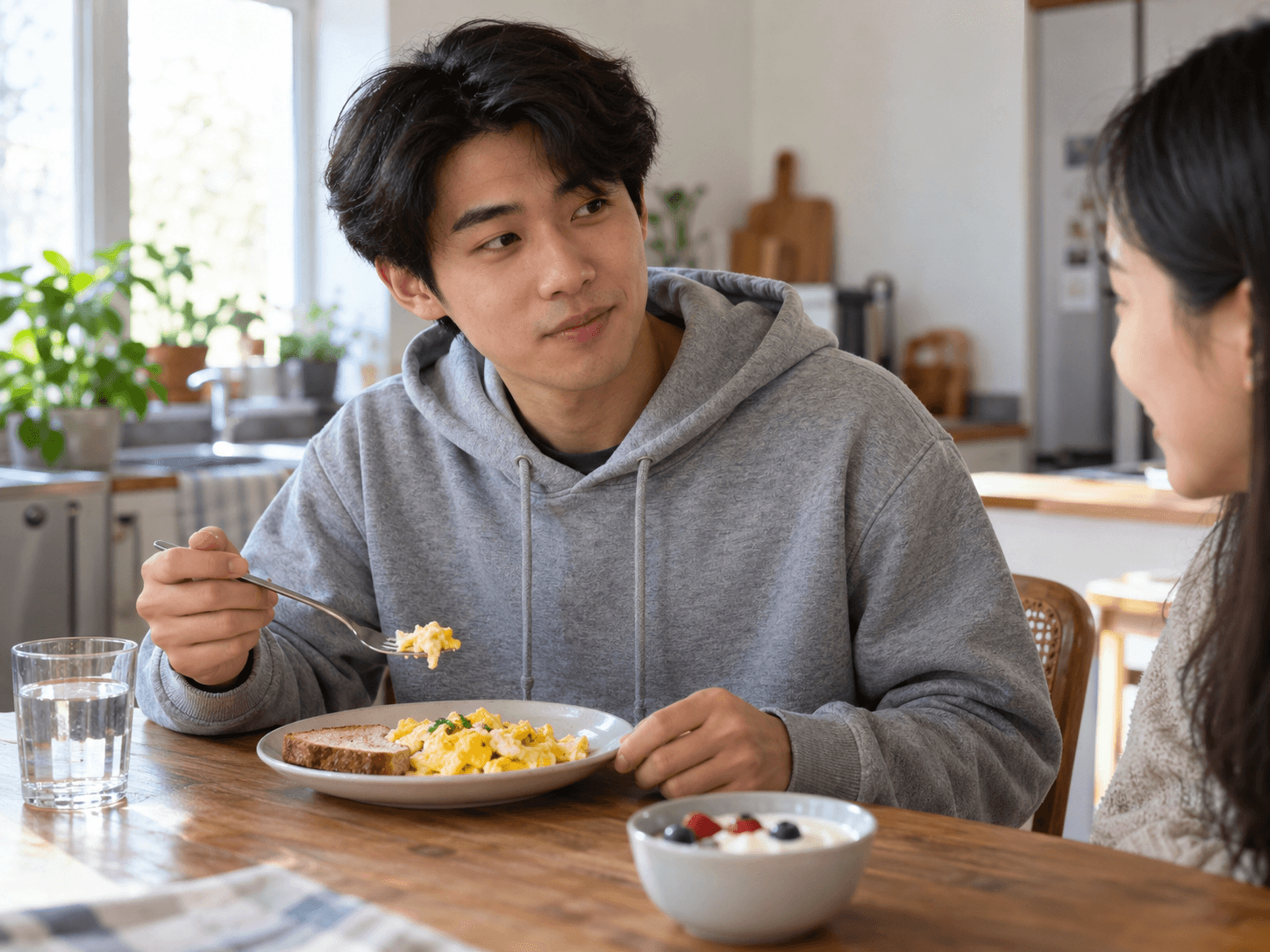 A young adult eats scrambled eggs while talking with his companion at breakfast.